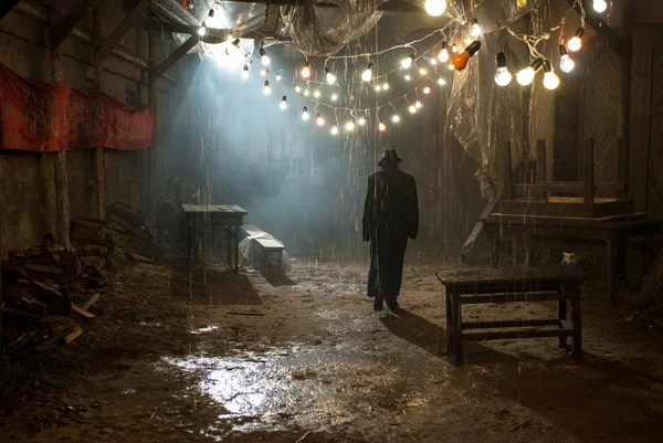 Hombre de sombrero negro bajo la lluvia en la oscura calle nublada —  Fotos de Stock