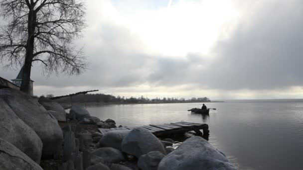 Fiskaren simmar på en gammal båt till steniga banken i skymningen — Stockvideo