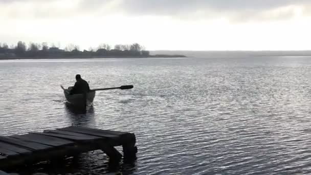 Рыбак плавает на старой лодке к каменистому берегу в сумерках — стоковое видео