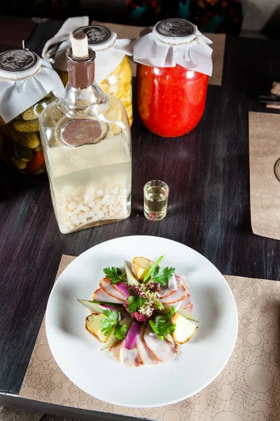 dish of meat and vegetables on the table in the restaurant. next to the bottle of alcohol and pickled cucumbers and tomatoes