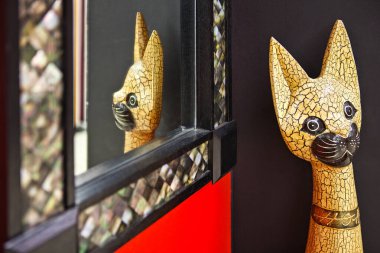 Koyu kırmızı arka planda aynada yansıması olan bir kedinin ahşap heykeli.