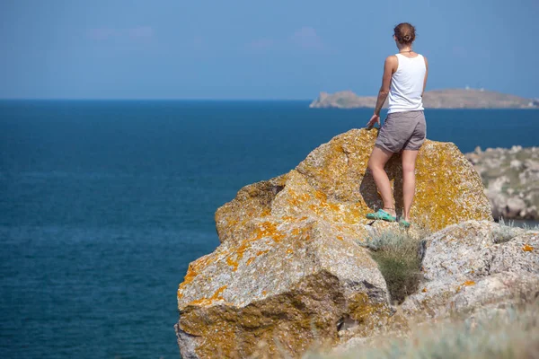 Joven turista rubia de pie sobre rocas naturales junto al mar al atardecer y mirando a un lado. Región mediterránea, Turquía — Foto de Stock