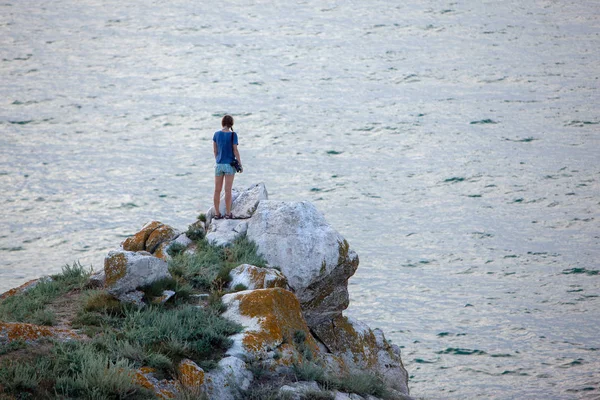 Jeune touriste blonde debout sur des rochers naturels au bord de la mer au coucher du soleil et regardant de côté. Région méditerranéenne, Turquie — Photo