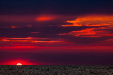 Bulutlu bir gökyüzünde deniz üzerinde güzel kırmızı ve turuncu gün batımı. Güneş denizin üzerinden battı. İki martı gün batımına karşı uçuyor. Dramatik Günbatımı Gökyüzü