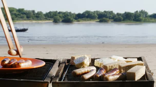Grill - grillowanie kiełbasek i tofu na plaży nad rzeką - 4k — Wideo stockowe