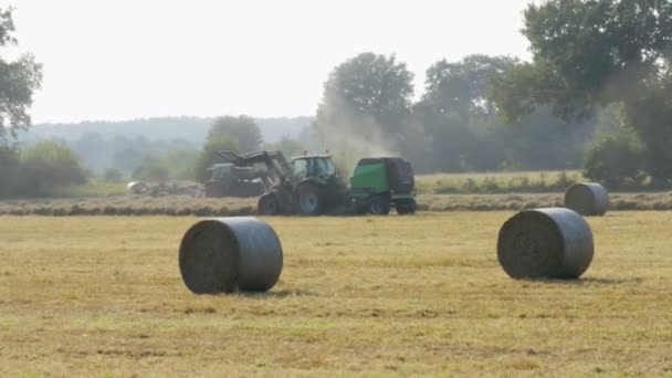 Trator corre no campo no outono e reúne feno em fardos — Vídeo de Stock