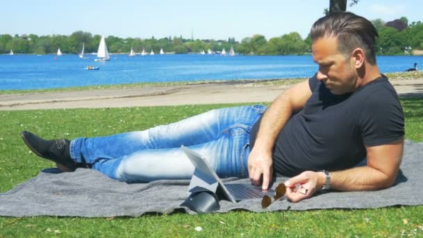 Выходные в городе - мужчина отдыхает на траве в парке и занимается серфингом в Интернете — стоковое видео