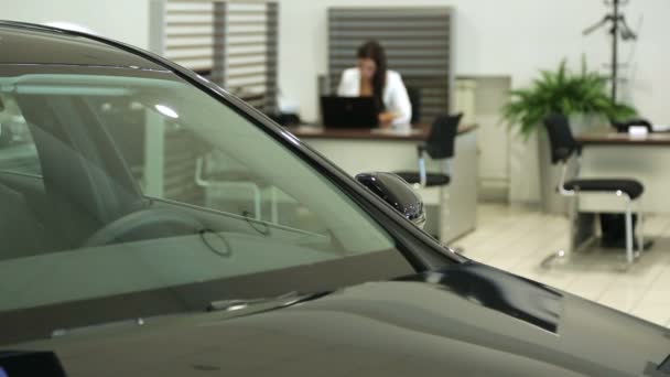 Trabaja en la sala de exposición. El gerente de ventas del concesionario trabaja en un escritorio. En el primer plano del coche, el gestor de imágenes está borroso . — Vídeos de Stock