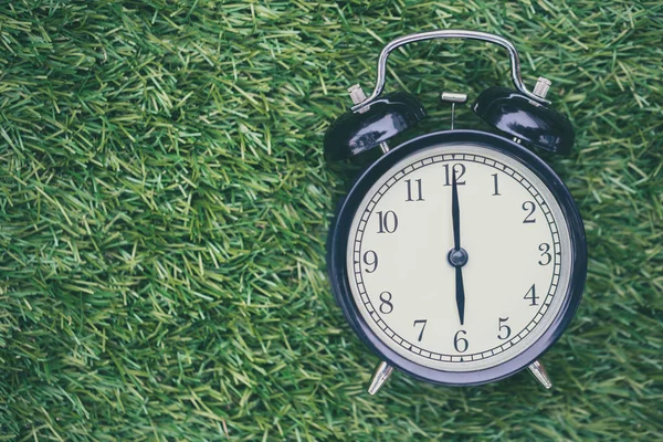 Times retro clock lay on green grass nature face timed at 6 o'clock morning time for background or postcard. — Stock Photo, Image