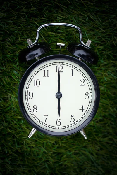 Closeup tijden retro klok leggen op groen gras natuur gezicht getimed om 6 uur donkere nachttijd voor achtergrond of briefkaart. — Stockfoto