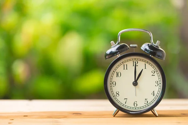Часы на деревянном столе в зеленом саду время в 1 час — стоковое фото