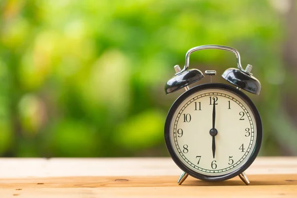 Часы на деревянном столе в зеленом саду время в 6 часов — стоковое фото