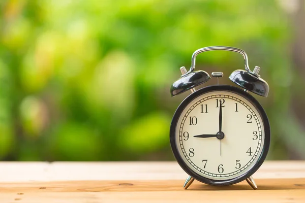 Часы на деревянном столе в зеленом саду время в 9 часов — стоковое фото