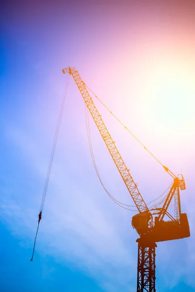 Bouw hijsen kranen silhouet tegen blauwe hemel met zon achtergrond. — Stockfoto