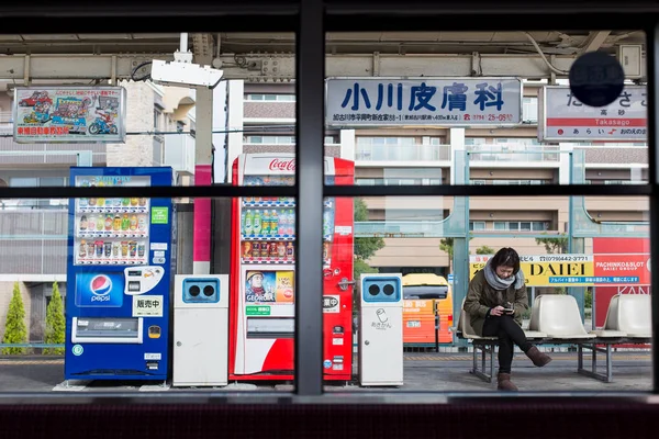 Giapponese signora attesa da solo guardando smart phone a stazione ferroviaria piattaforma . — Foto Stock