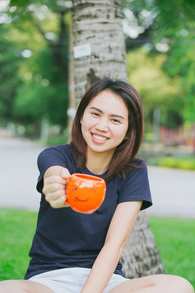 Aziatische tiener handvat glimlach mok in het groene park. Gelukkig drinken koffie concept. — Stockfoto
