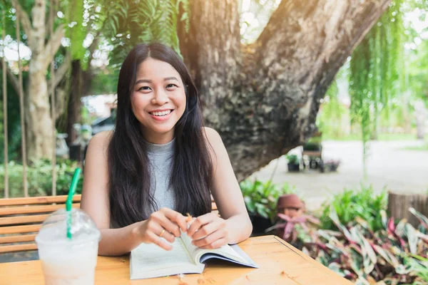 Happy keer met leesboek, Aziatische vrouwen Thaise tiener glimlach met boek in de tuin met coffeeshop ontspannen. — Stockfoto