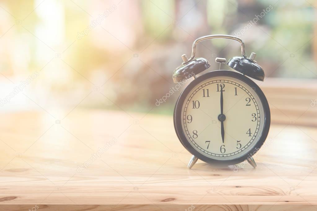 Retro clock at 6 o'clock on wood table foreground with blur light nature background