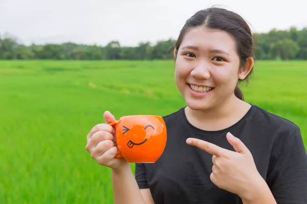 Asiatico carino giovanissima ragazza sorriso dito puntare a tazza con verde riso campo fondo buono wheatgrass bevanda concetto — Foto Stock