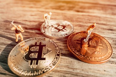 Bit madencisi ya da Bitrig konsepti için ahşap arka planda Bitcoin 'leri olan minyatür insanlar para işçisi.