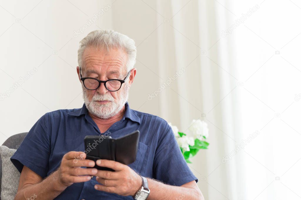 elder gray beard white hair with glasses looking attention at his smartphone to reading news at home alone.