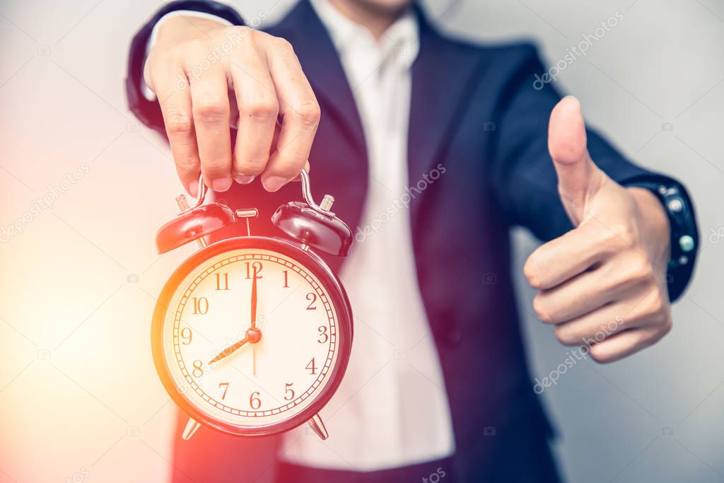 Business person hand showing thumbs up with a clock for good times or right time work on time concept.