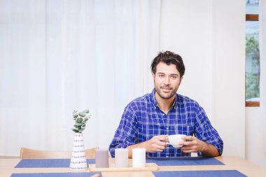 Mutfak masasında oturan yakışıklı adam sıcak içecek ya da mesaj için beyaz alan olan kahve içer..