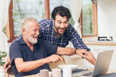 Yaşlı adam gülümsemesi, oğluyla birlikte dizüstü bilgisayara baktığı için mutlu. İletişim teknolojisini aile mutluluğu için kullanmak diğer kavramları bağlamak için yaşlı ev bakımı