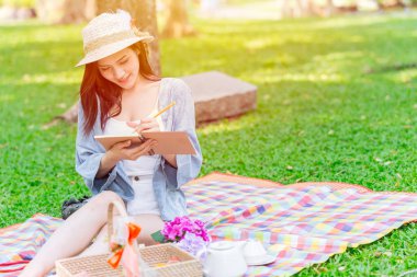 Güzel Asyalı kız Green Park 'ta tek başına piknik yaparken günlüğü ve yazıları not alıyor.