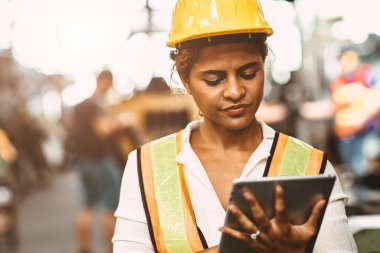 Ağır endüstri bakım mühendisi Amerikalı kadın işçi güvenlik üniforması ve miğfer giyerek fabrikadaki kontrol makinesine tablet bilgisayar kullanarak çalışmaktan memnun..