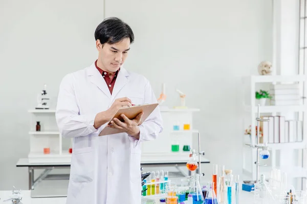 Asian Male Scientist Doctor pay attention working in lab hand taking note or research writing list of medical formula sample.