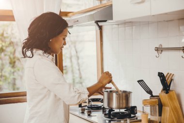 Afro-Amerikalı siyahi kadın evdeki mutfakta kaynar çorba pişiriyor..