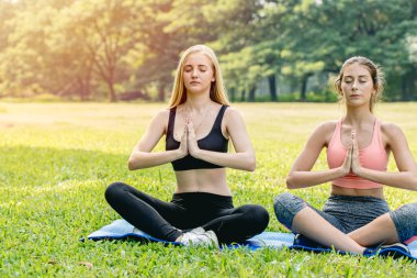 Güzel kızlar, genç arkadaşlar yogayı yeşil parkta sağlıklı bir tatil için yaparlar. Lotus 'un gözleri kapalı konsantrasyon duruşunda otururlar..