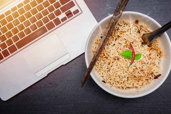 Instant noodle with computer laptop for low cost cheap eat and unhealthy high carbohydrate food concept.