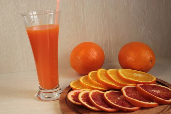 Orange juice in a glass, and oranges cut into circles on a platter.