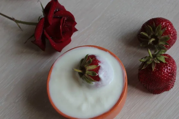 Red rose and strawberry with cream on a light background.