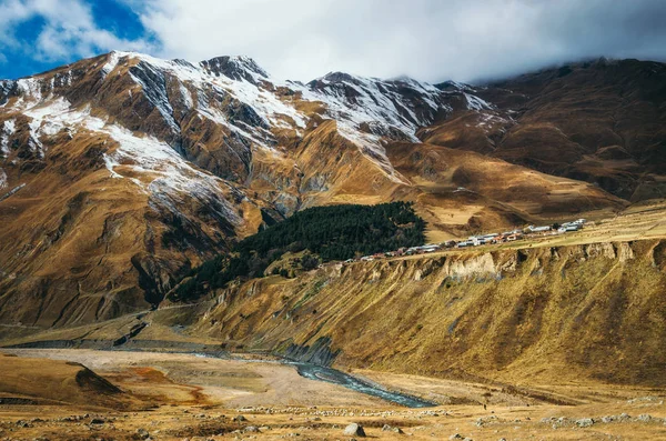 Pueblo en la colina de las montañas del Gran Cáucaso con picos nevados glaciar en Kazbegi, Georgia — Foto de Stock