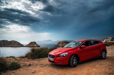 Kırmızı araba Volvo v40 fırtınalı gökyüzü karşı bir uçurumun kenarında duran.
