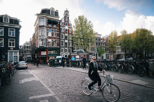 Adult woman rides a bicycle in historical part of Amsterdam with typical traditional houses. — Stock Photo, Image