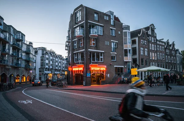 Adult rides a bicycle in historical part of Amsterdam against the coffeeshop with legal drugs in evening. — Stock Photo, Image