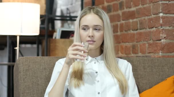 Kvinna dricksvatten i glas, sitter på soffa — Stockvideo