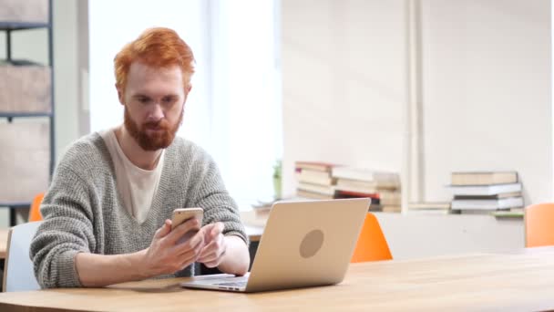 Чоловік за допомогою смартфона, перегляд онлайн на роботі — стокове відео