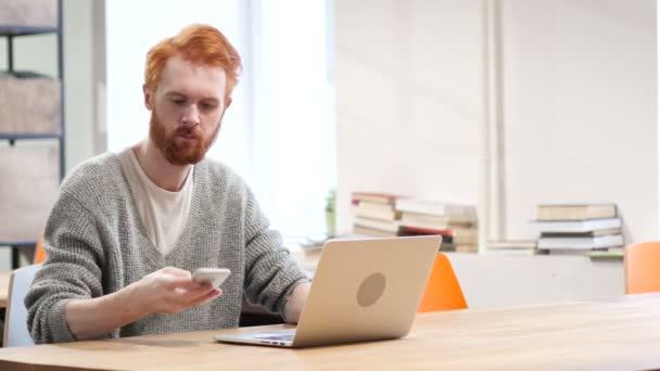 Hombre que asiste a la llamada telefónica, trabajando en el ordenador portátil — Vídeos de Stock