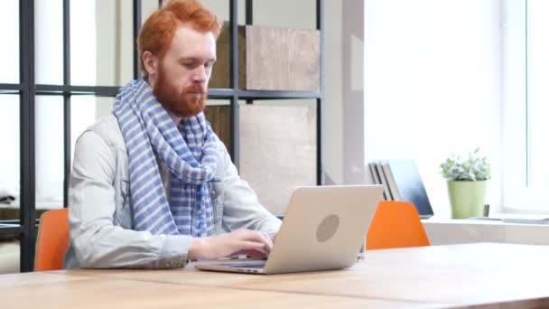 Hombre mirando hacia la cámara mientras trabaja en el ordenador portátil — Vídeos de Stock
