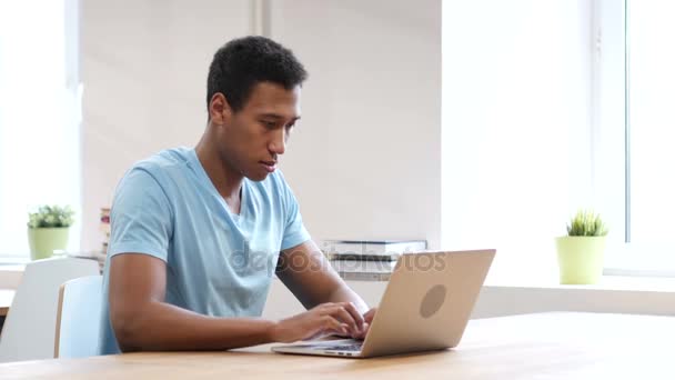 Серйозний чорний чоловік дивиться на камеру, працює на ноутбуці — стокове відео