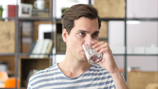 Schöner Geschäftsmann in lässigem Tuch, der im Büro Wasser trinkt — Stockfoto