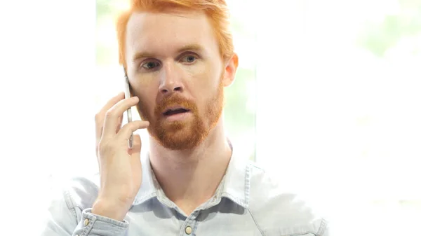 Говоря по телефону, молодой рыжий бородач обсуждает новый проект — стоковое фото
