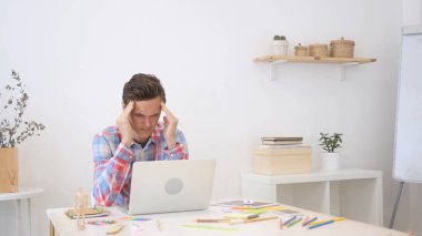 Genç yaratıcı tasarımcı adam yaratıcı ofisinde çalışan baş ağrısı ile