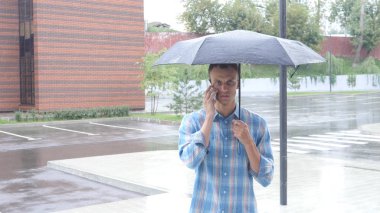 Şemsiyenin altına yağmur sırasında ayakta telefonda konuşuyor