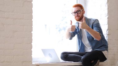 Thumbs Up penceresinde kırmızı saç ve sakal ile oturan adam, çalışarak
